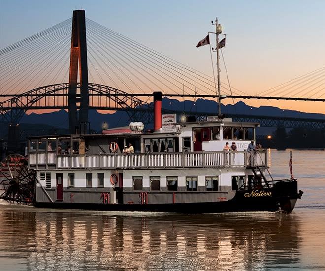 MV Native paddlewheeler cruising at sunset under the SkyTrain bridge on the Fraser River